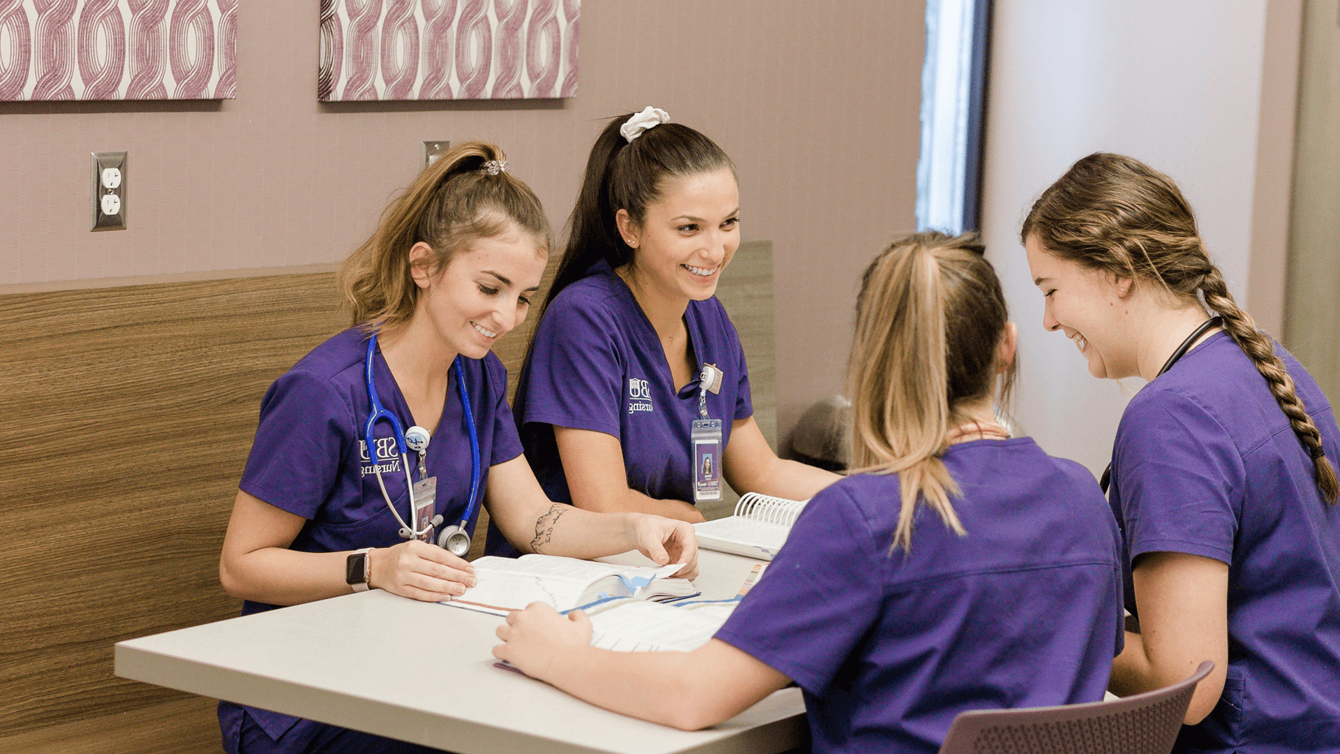 四个穿着紫色工作服的女孩笑着坐在桌子旁一起学习